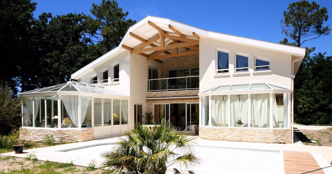 Grande maison contemporaine à étage avec deux vérandas, un balcon vitré et une terrasse ensoleillée.