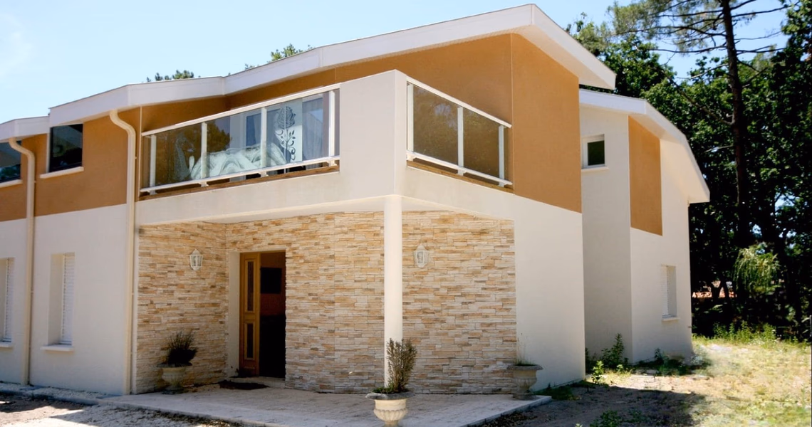 Façade contemporaine en enduit blanc et ocre avec porche en pierre de parement et balcon à l'étage.