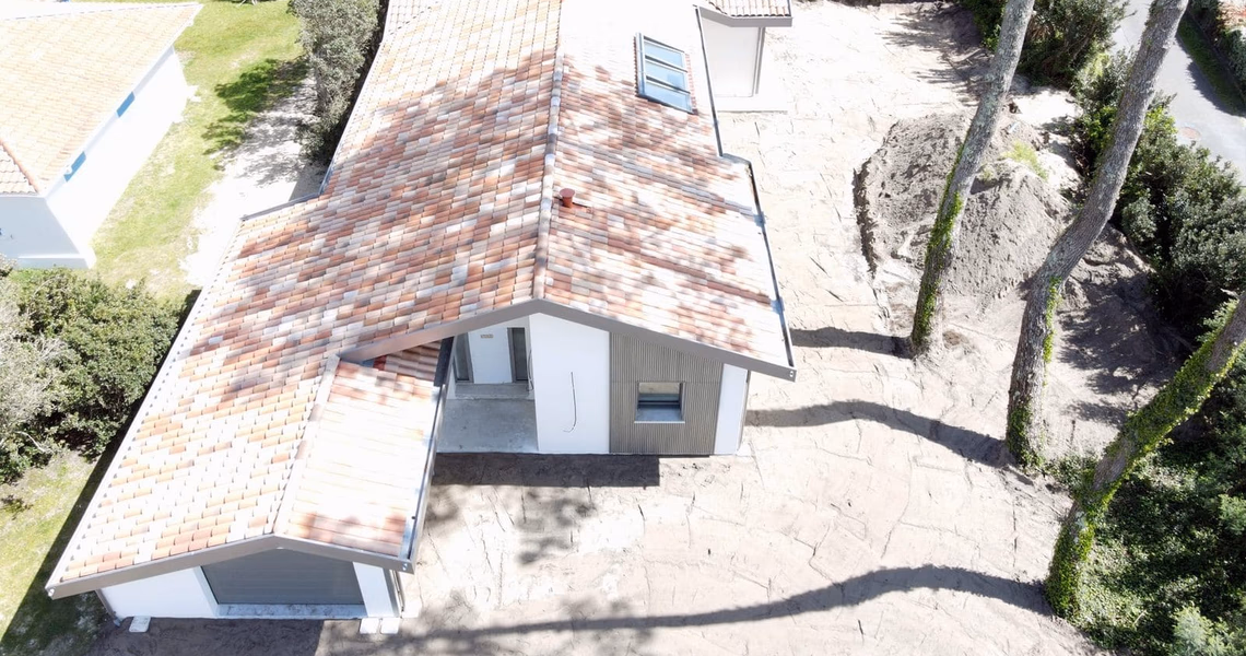 Vue aérienne d'une maison en construction avec toiture en tuiles et terrain paysagé de pins.
