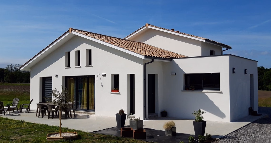Façade de la villa blanche à étage avec toiture en tuiles, grandes baies vitrées et terrasse aménagée.