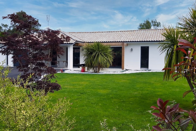Maison moderne de plain-pied à toiture en tuiles avec façade blanche, jardin paysager et pelouse.