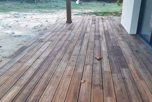 Terrasse en bois lambris posée le long de la façade blanche d'une maison neuve avec jardin en terre.