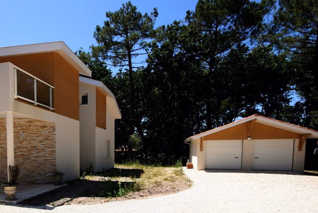 Façade de la maison contemporaine à étage avec parement en pierre, balcon et garage indépendant.