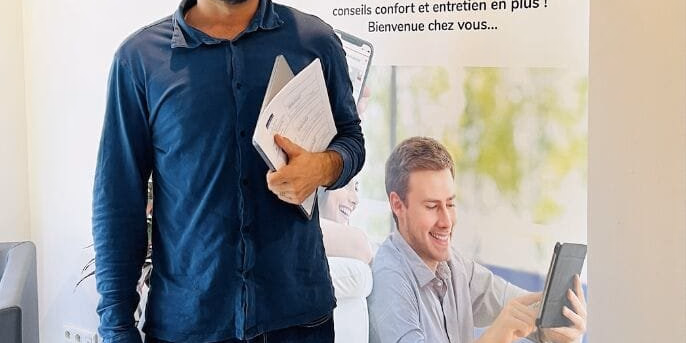 Un homme souriant debout tient des dossiers devant un roll-up promotionnel My Landes Habitat.