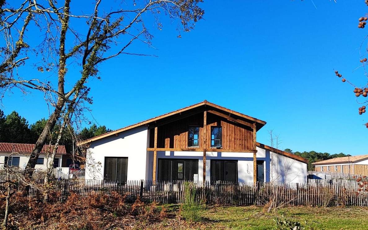 Villa contemporaine avec murs blancs et bardage en bois, entourée d'arbres sous un ciel bleu.