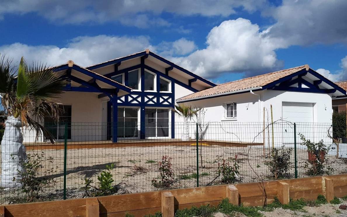 Façade de villa moderne blanche aux charpentes bleues, toiture en tuiles et grand garage attenant.