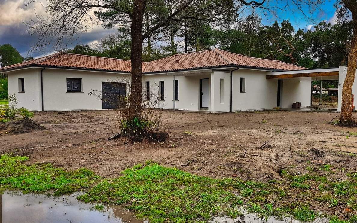 Maison de plain-pied blanche à toiture en tuiles avec grand carport et terrain en cours d'aménagement.