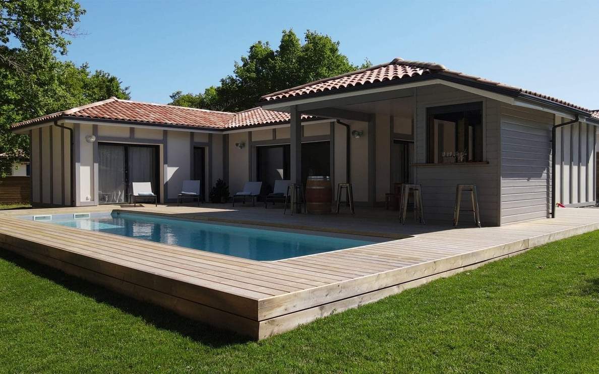 Maison de plain-pied moderne avec piscine rectangulaire encastrée dans une vaste terrasse en bois.