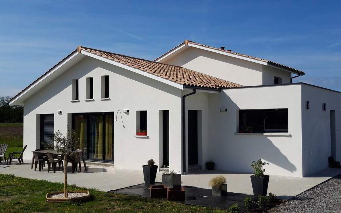 Façade de la villa moderne avec enduit blanc, toiture en tuiles et grande terrasse aménagée.