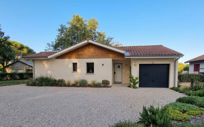 Façade avant de la maison de plain-pied à Herm avec bardage bois sous pignon, cour gravillonnée et garage anthracite