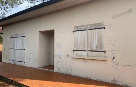 Mur extérieur d'une maison avec des fenêtres en bois fermées et un chemin en pavés.