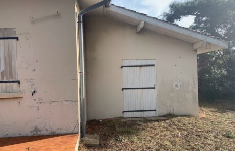 Mur extérieur d'une maison avec une porte blanche et des volets en bois fermés.
