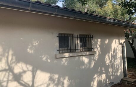 Mur extérieur d'une maison avec des fenêtres protégées par des grilles en métal.