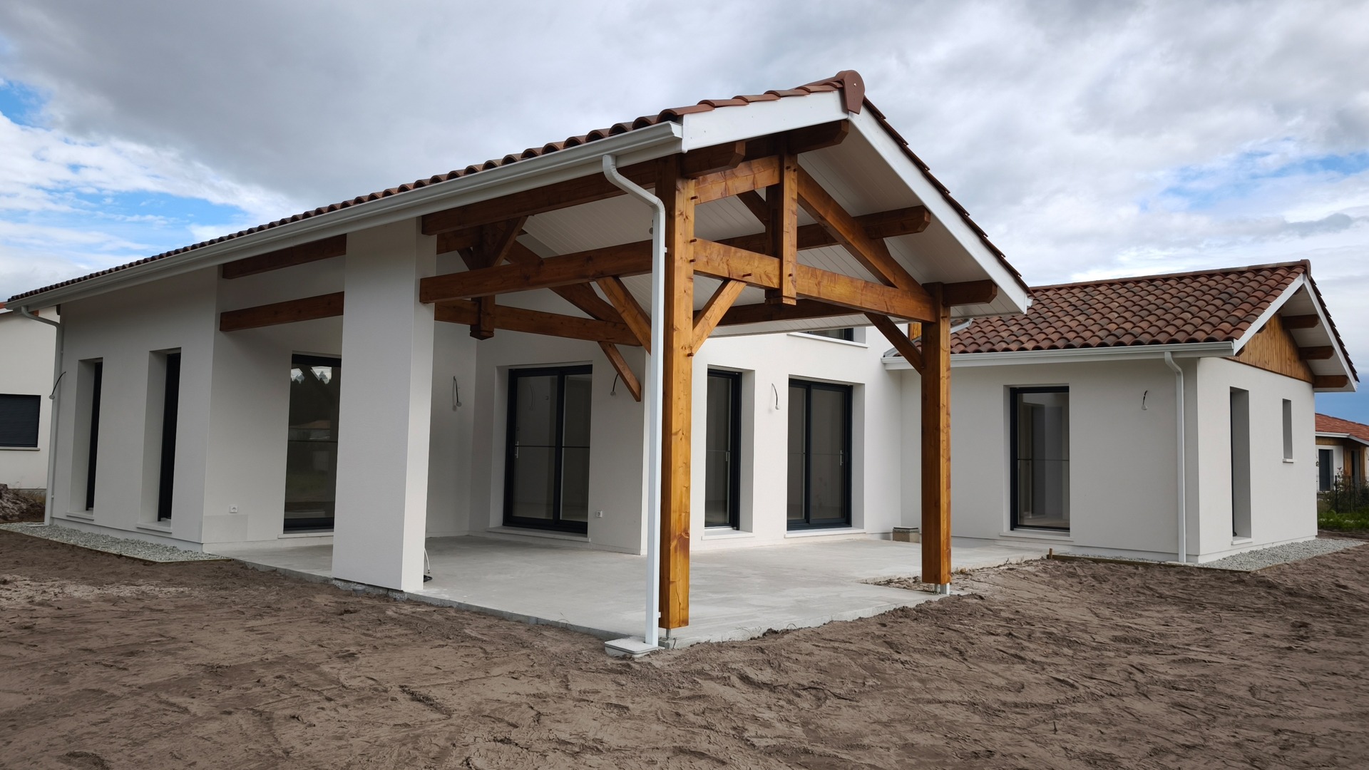 Vue de la terrasse couverte de 44.23m² en béton avec sa charpente traditionnelle en sapin, donnant sur la pièce de vie de la maison de Vielle-Saint-Girons.