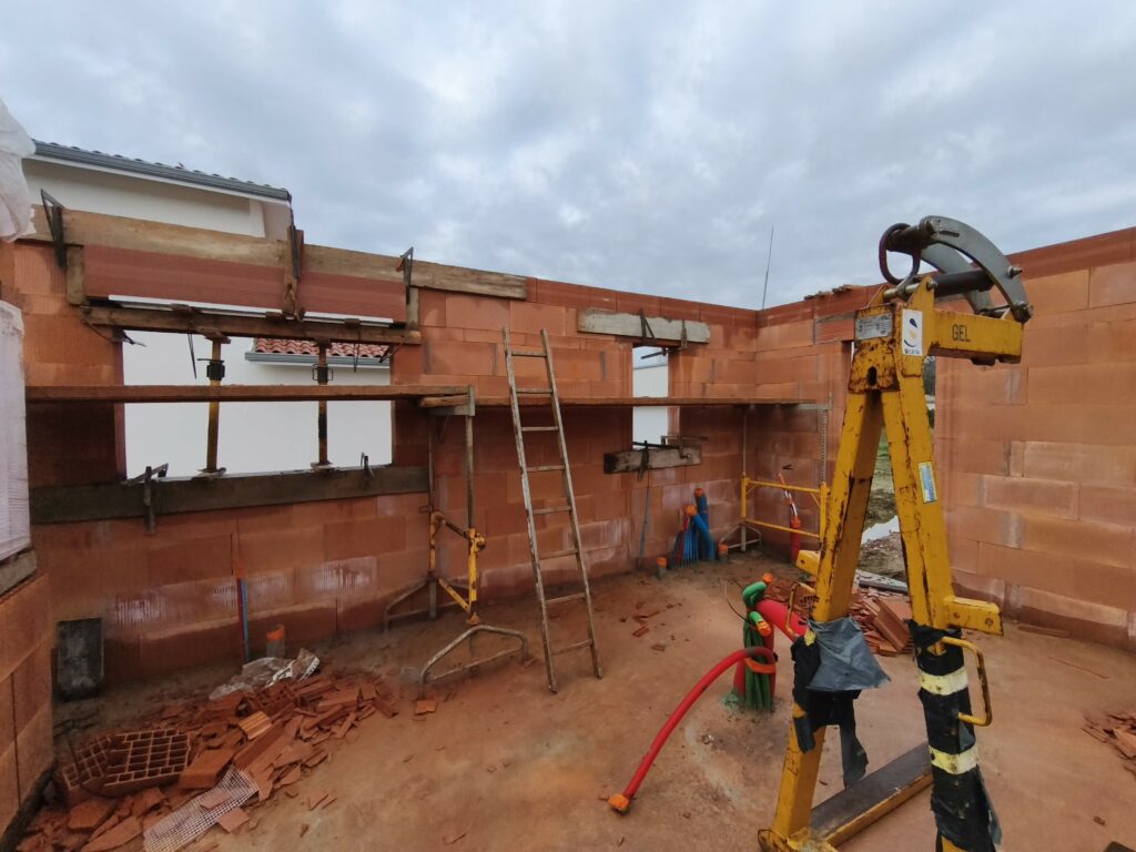 Intérieur d'un chantier avec élévation des murs en briques rouges et coffrage des linteaux de fenêtres.