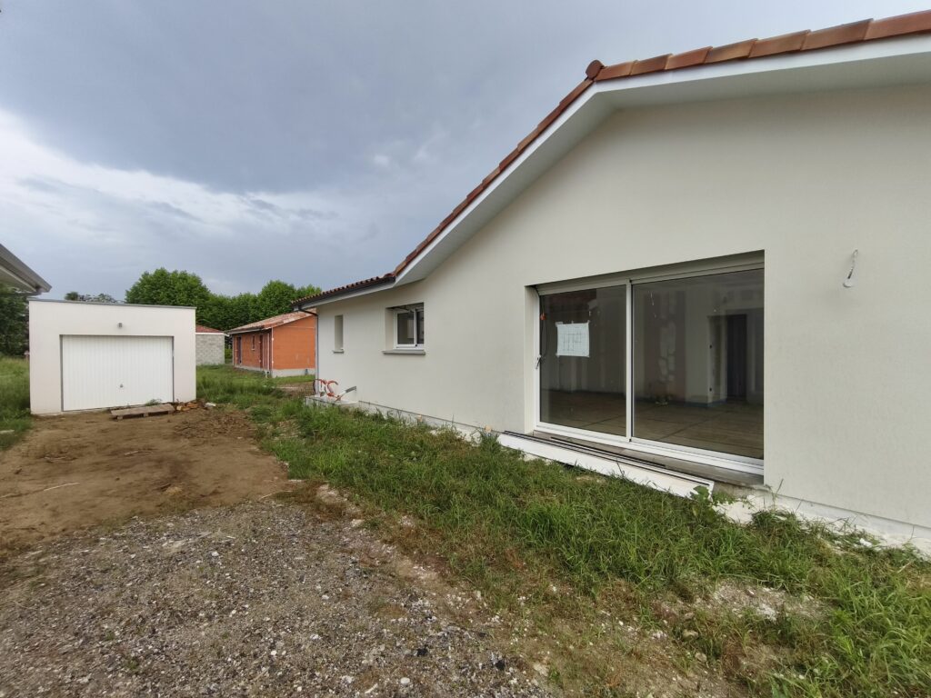 Grande baie vitrée coulissante en aluminium sur la façade arrière d'une maison contemporaine avec garage indépendant.