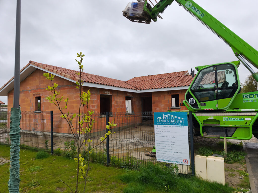 Maison individuelle hors d'eau avec toiture terminée et engin de levage sur le chantier